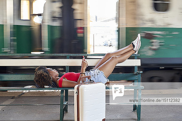 Frau mit Koffer auf einer Bank am Bahnhof liegend
