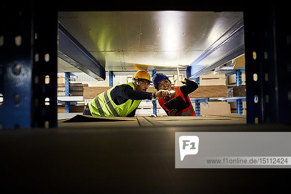 Zwei Arbeiter mit Taschenlampe suchen etwas im Fabriklager