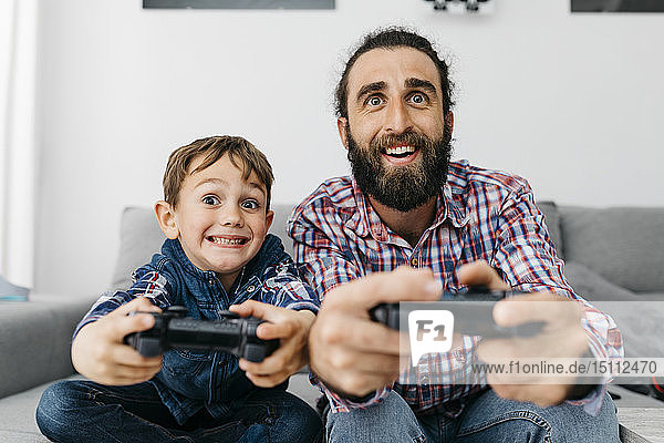 Porträt von Vater und Sohn  die zusammen auf der Couch sitzen und ein Computerspiel spielen