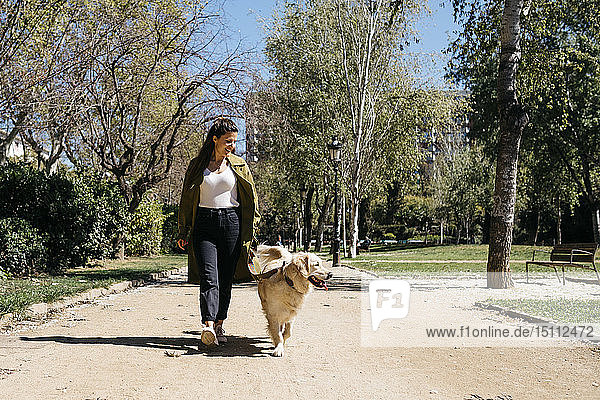 Glückliche Frau geht mit ihrem Labrador Retriever im Stadtpark spazieren