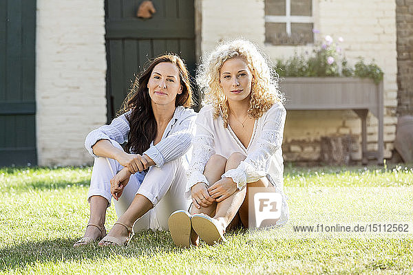 Zwei Frauen sitzen im Garten auf Gras im Sonnenschein