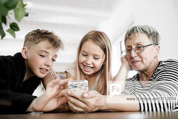 Glückliche Großmutter und Enkelkinder telefonieren zu Hause