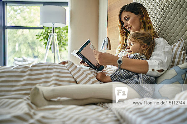 Mutter und Tochter lesen ein Buch im Bett
