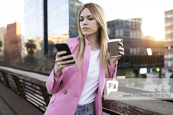 Junge Geschäftsfrau benutzt Smartphone und hält Kaffee zum Mitnehmen
