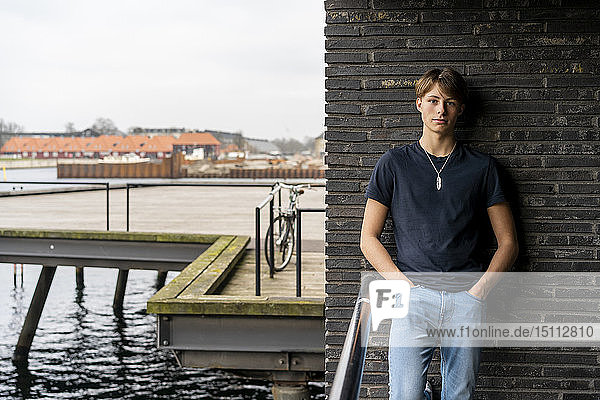 Dänemark  Kopenhagen  Porträt eines jungen Mannes  der an einer Wand am Wasser stehend gelehnt ist