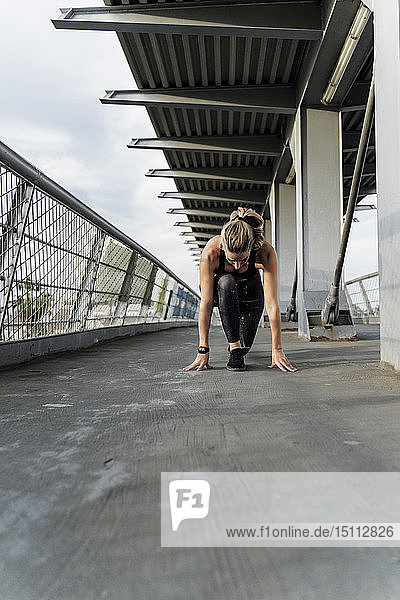 Sportliche Frau in Startposition auf einer Brücke  beginnt zu laufen