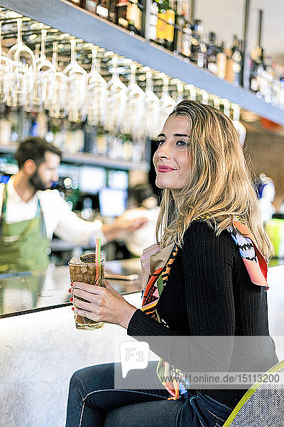 Lächelnde Frau mit einem Cocktail  die an der Theke einer Bar sitzt