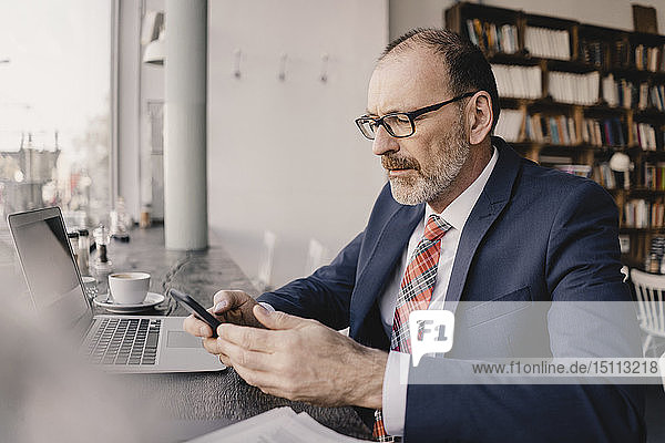 Ein reifer Geschäftsmann benutzt Handy und Laptop in einem Café