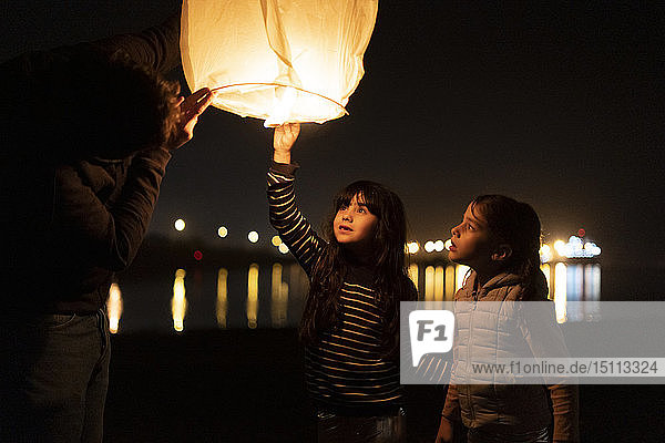 Father and two girls preparing a sky lantern on the beach at night