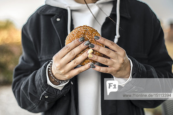 Hände einer jungen Frau mit bemalten Nägeln  die einen Hamburger hält  Nahaufnahme
