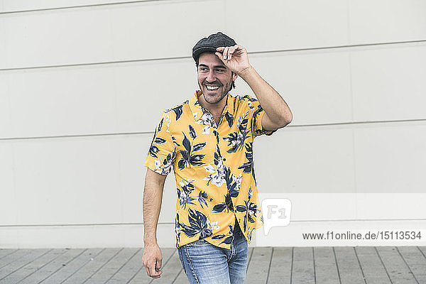 Junger Mann mit flachem Hut und Aloha-Hemd  lacht vor der Wand