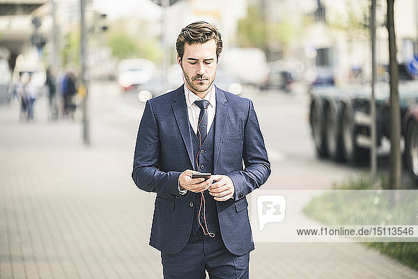 Businessman walking in the city using cell phone