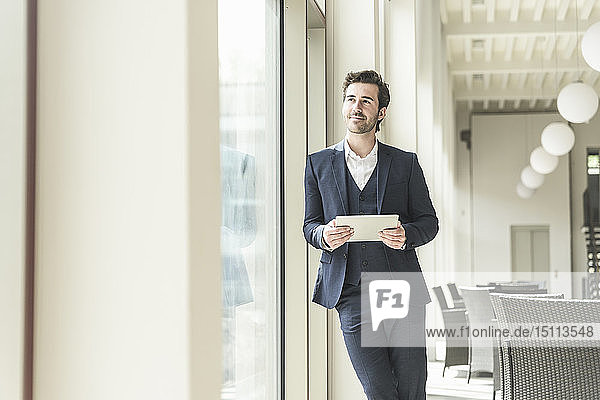 Junger Geschäftsmann steht im Bürogebäude und benutzt ein digitales Tablet