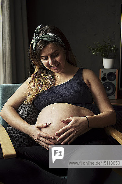 Schwangere  die zu Hause auf ihren Babybauch schaut