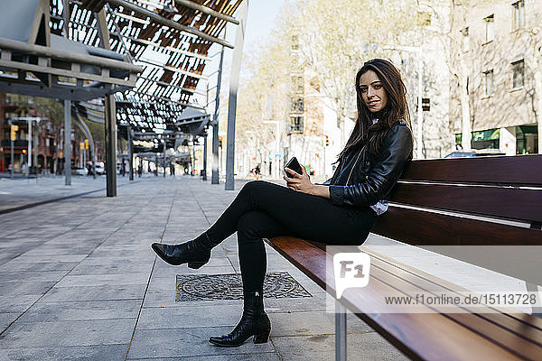 Junge Frau sitzt auf einer Bank und hält ihr Smartphone