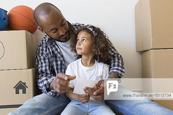 Father and daughter sitting on the floor at new home surrounded by cardboard boxes