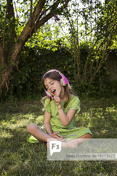 Portrait of girl sitting on meadow listening music with headphones and smartphone