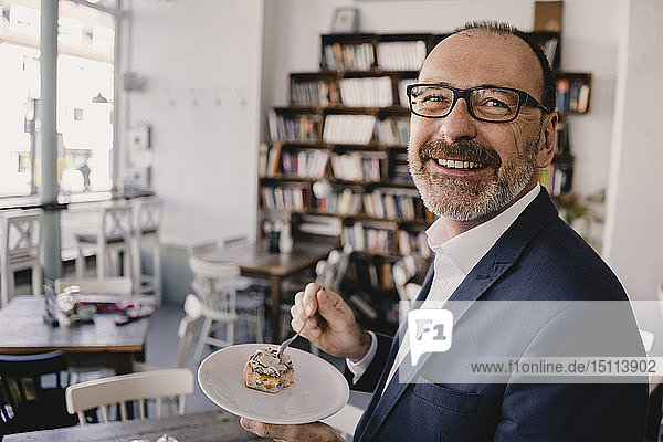 Smiling mature businessman having a piece of cake in a cafe