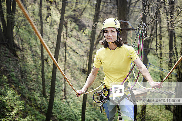 Junge Frau mit gelbem T-Shirt und Helm in einem Seilgarten