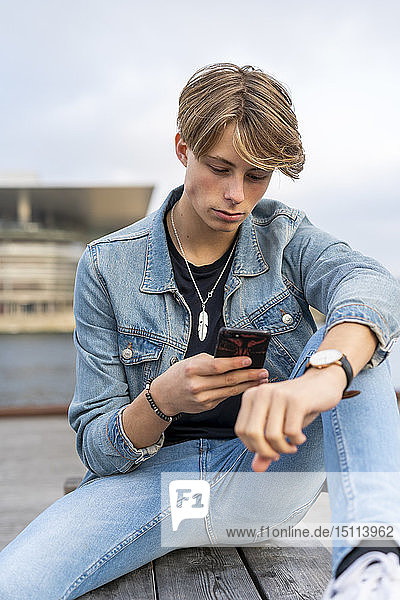 Dänemark  Kopenhagen  junger Mann sitzt auf einer Bank am Wasser und telefoniert