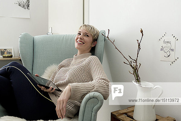Glückliche Frau sitzt zu Hause im Sessel mit Tablette