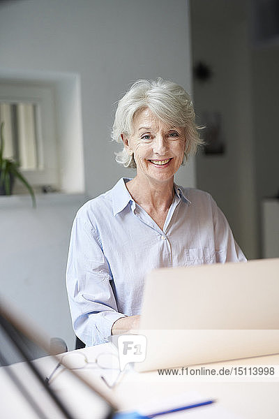 Porträt einer lächelnden reifen Frau mit Laptop am Schreibtisch