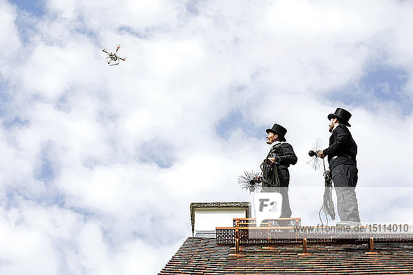 Zwei Schornsteinfeger auf dem Hausdach betrachten Drohne