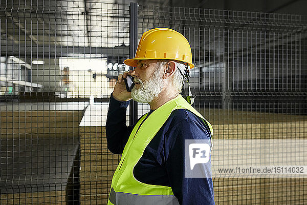 Älterer Arbeiter am Handy im Fabriklager