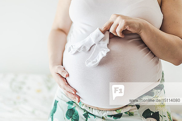 Mittelteil einer schwangeren Frau  die Babysocken hält