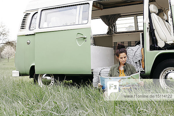 Young woman studying map  sitting in the grass  in front of her camper