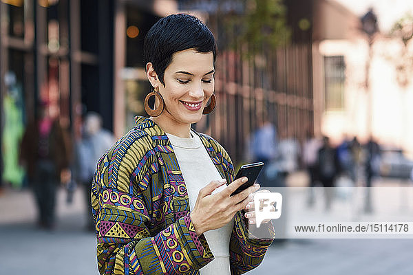 Lächelnde  modische junge Frau benutzt Mobiltelefon in der Stadt