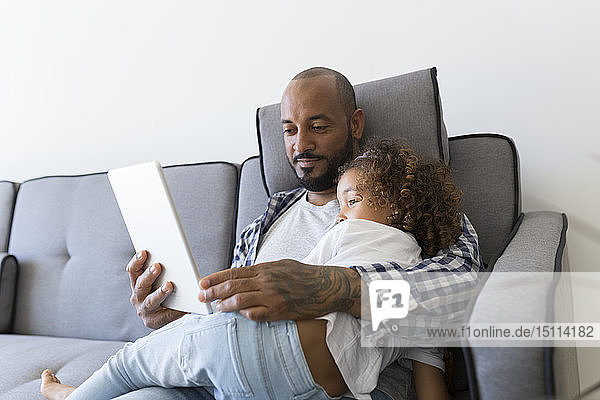 Father and daughter sitting on couch at home together looking at tablet