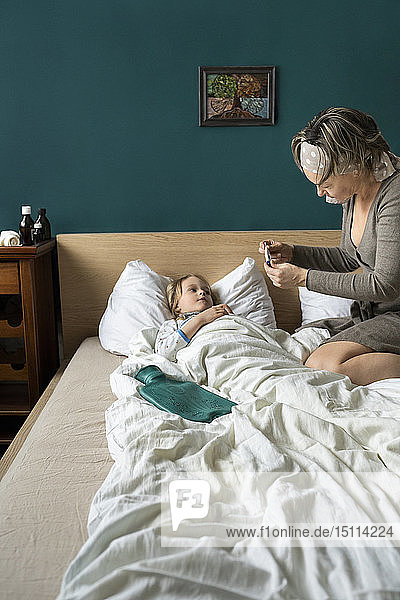 Mutter nimmt Temperatur einer kranken  im Bett liegenden Tochter