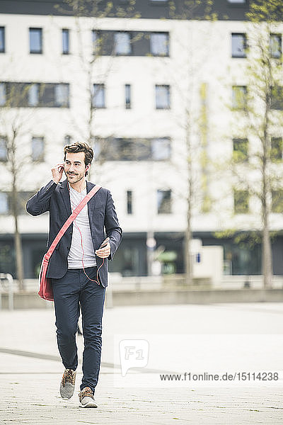 Businessman walking in the city with cell phone and earphones