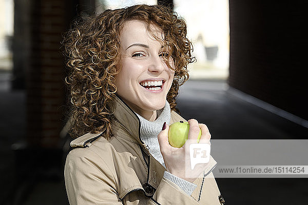 Bildnis einer lachenden Frau mit lockigem Haar mit grünem Apfel