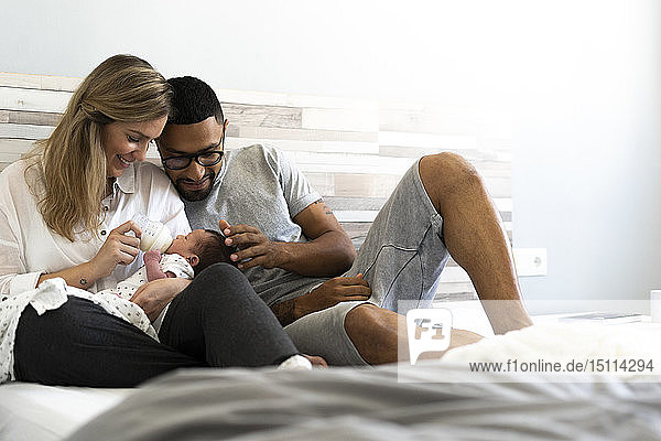 Happy father and mother bottle-feeding their newborn baby in bed