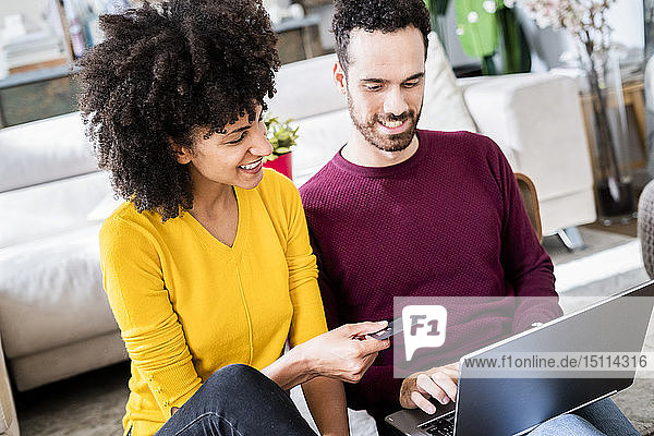Glückliches Paar zu Hause beim Online-Shopping mit Laptop und Kreditkarte