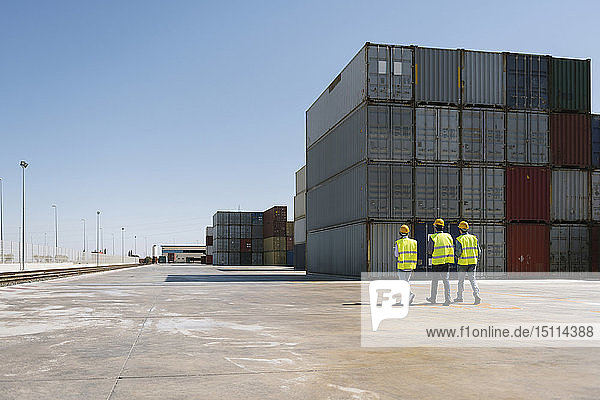 Arbeiter gehen gemeinsam in der Nähe eines Stapels von Frachtcontainern auf einem Industriegelände