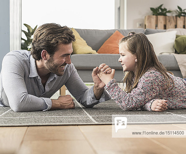 Young man and little girl lying on ground  arm wrestling