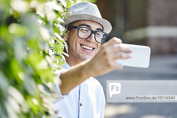 Porträt eines jungen glücklichen Mannes  der mit einer Hecke im Hintergrund Selbsthilfe nimmt