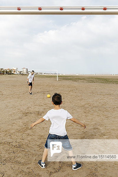 Junge und Mann spielen Fussball am Strand