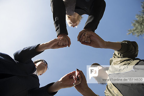Blick aus der Froschperspektive auf drei Frauen  die unter blauem Himmel Händchen halten