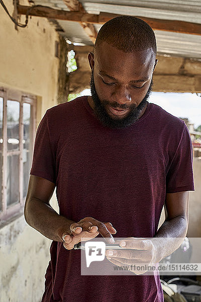 Mosambik  Maputo  junger Mann auf der Veranda mit Smartphone