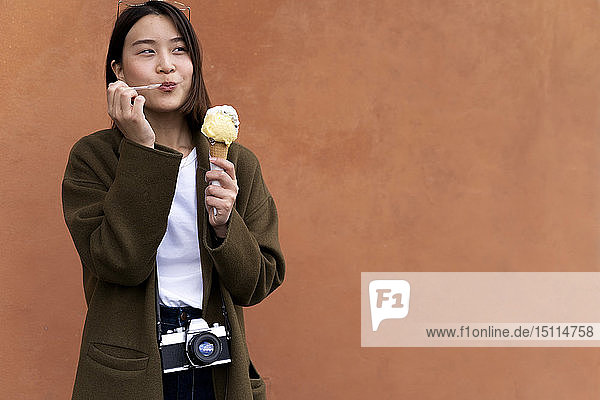 Young woman eating an ice cream cone at an orange wall