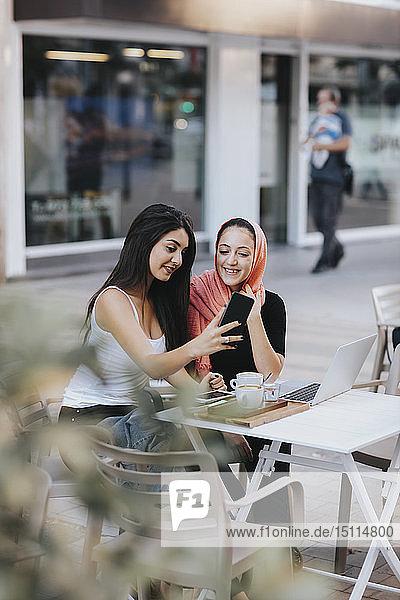 Zwei Freunde sitzen mit dem Handy in einem Straßencafé zusammen