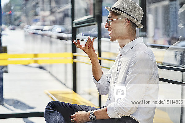Glücklicher junger Mann benutzt Handy an einer Straßenbahnhaltestelle in der Stadt
