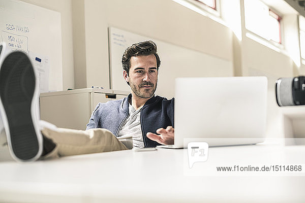Young businessman working relaxed in modern office  using laptop with feet on desk