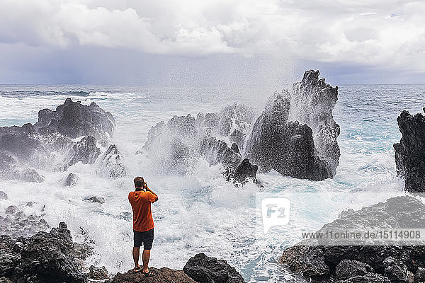 USA  Hawaii  Big Island  Laupahoehoe Beach Park Mann fotografiert brechende Brandung an der felsigen Küste