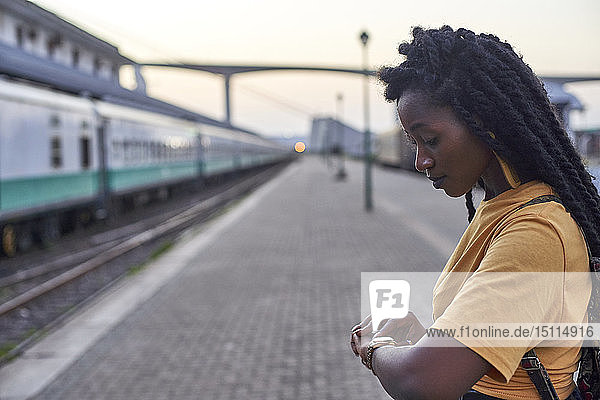 Junge Frau auf dem Bahnsteig des Bahnhofs  die ihre Uhr kontrolliert