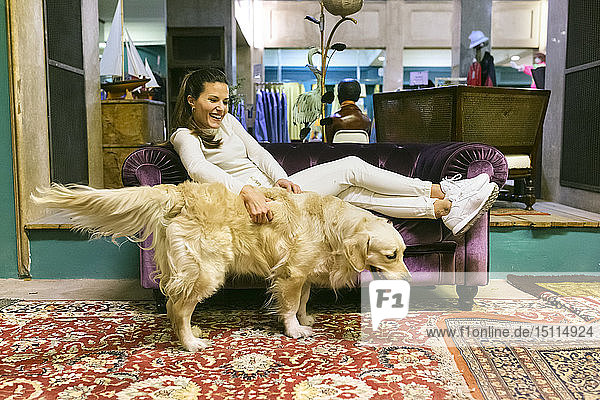 Lächelnde Frau mit Hund liegt auf der Couch in einem Vintage-Laden